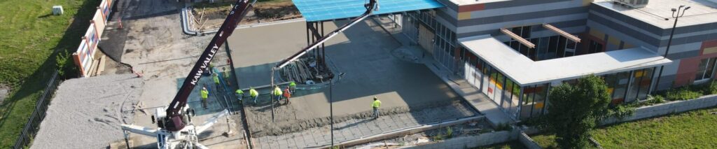 Aerial view of construction workers pouring concrete at a building site with a colorful facade under a clear blue sky.