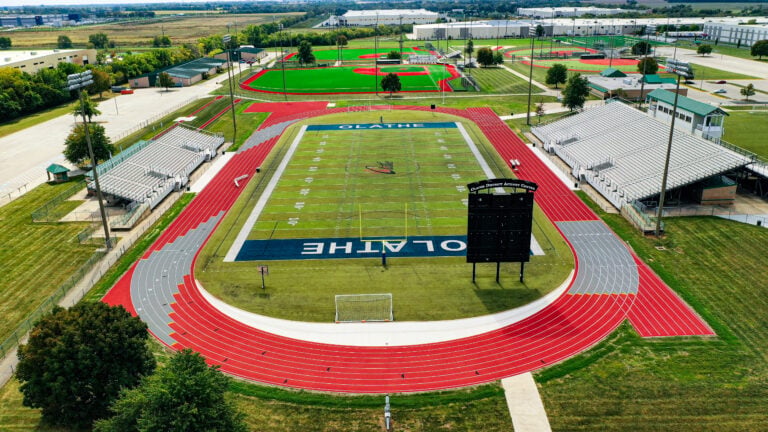 Aerial view of Olathe's football field and track, flanked by bleachers with a baseball field in the background.
